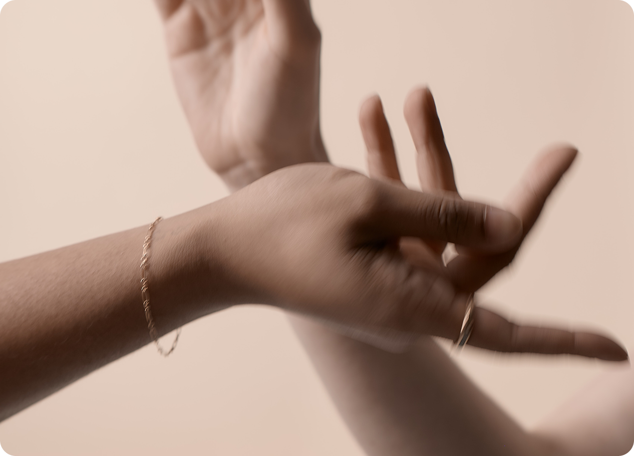 Two hands crossing over before a solid tan background. The hands are slightly blurred.